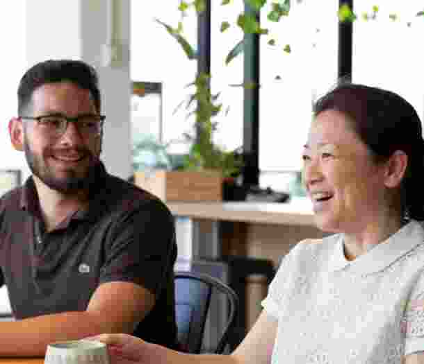 Two people sitting at cafe table. Both people are smiling.