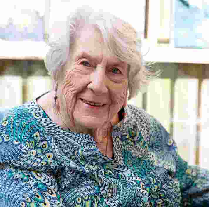 An older adult sitting in a chair smiling at the camera.