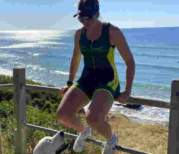 Al Viney sits on a fence at the beach in her training uniform. Charlie sits at her feet.