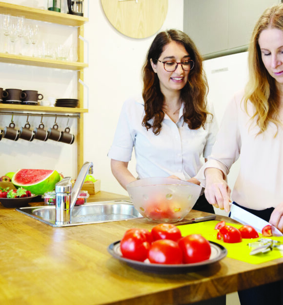 An occupational therapist works with a client in the kitchen chopping tomatoes.