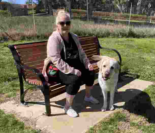 Leah sits on a park bench with her yellow Labrador guide dog Buzz