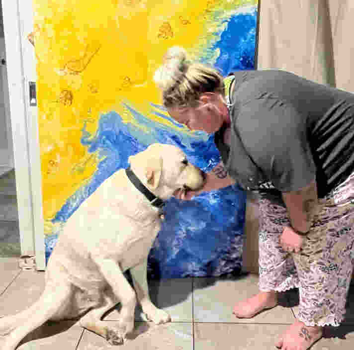 Leah cups Buzz's chin and leans towards him in front of her artwork