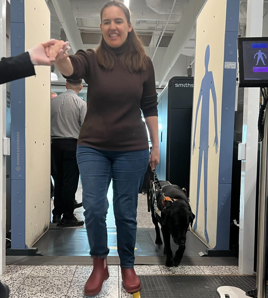 Erin and Guide Dog Jet are guided through a scanner at airport security.
