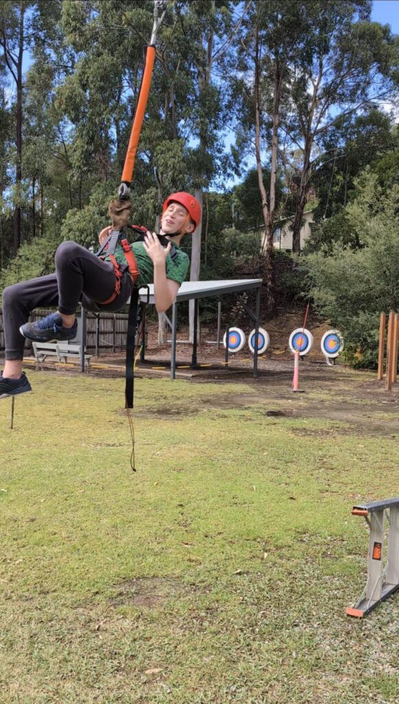 A participant wearing a red helmet, dangling from the flying fox with a smile on his face.  