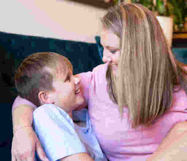 A mum has her arm around her son. Both are smiling at each other.