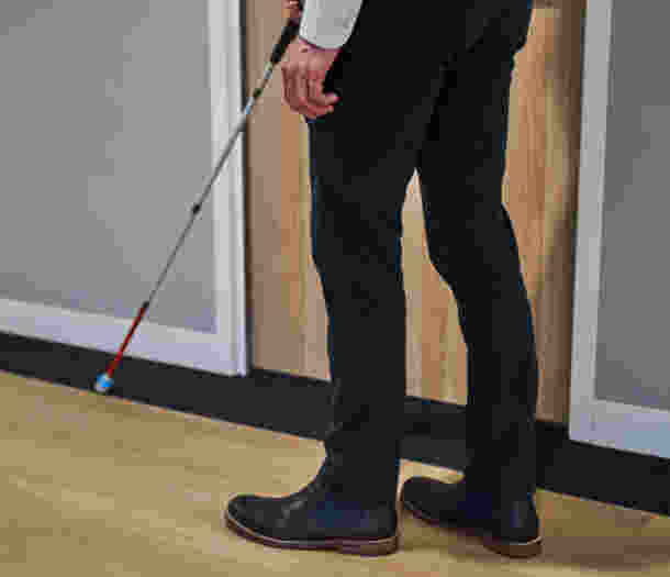 A close up image of a person's legs, using a white cane to navigate.