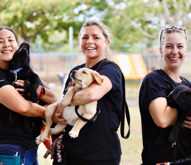 Three volunteers smiling at the camera, each holding a Labrador puppy.