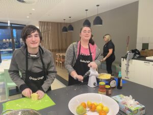 Two camp attendees help prepare dinner in the residential kitchen. One is cutting cheese and the other is grating cheese.