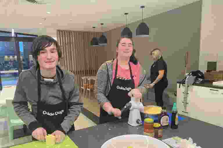 Two camp attendees help prepare dinner in the residential kitchen. One is cutting cheese and the other is grating cheese.