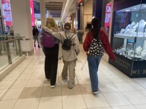 A group of three camp attendees walk in a row in a shopping centre. The middle person has their arm around the left person.