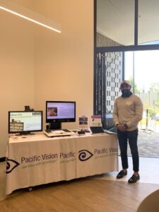 One of the assistive technology partners stands next to his display. Two computer screens stand on a table next to him.