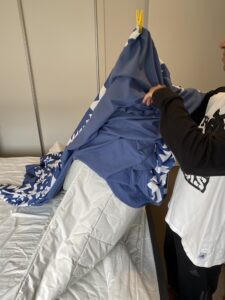 Matt standing in front of his unmade bed using a peg to mark the corner of his doona cover as a guide. He feeds a corner of the doona into the pegged corner.