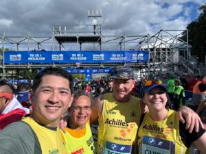 Four people stand in a crowd smiling into the camera after finishing the Berlin Marathon. The Brandenburg Gate is in view behind them.