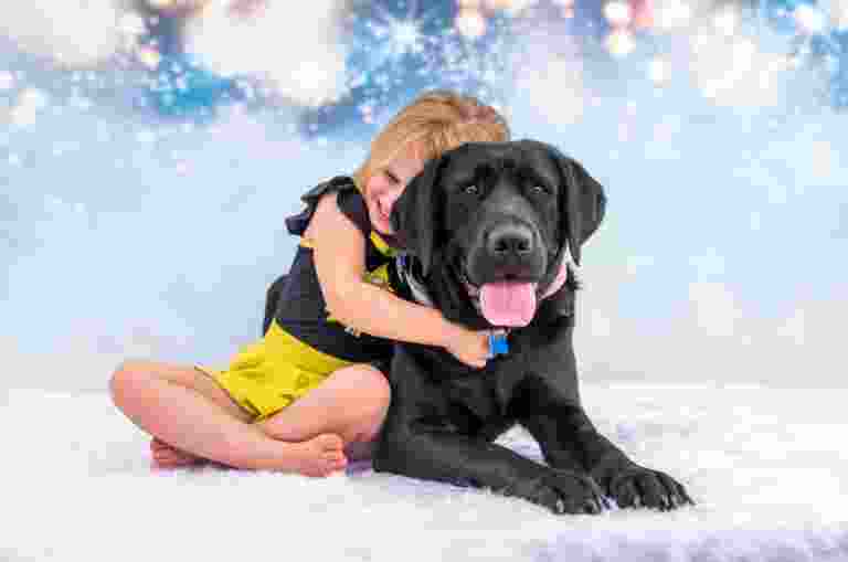 A young girl cuddles a black Therapy Dog on a fluffy white rug.