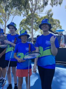 Three students holding white canes and tennis racquets ready for the blind tennis lesson. 