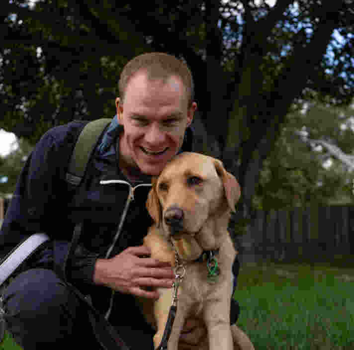 A man snuggling into his yellow Guide Dog, smiling at the camera.