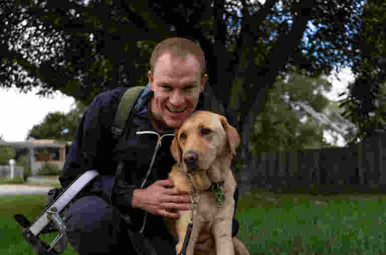 A man snuggling into his yellow Guide Dog, smiling at the camera.