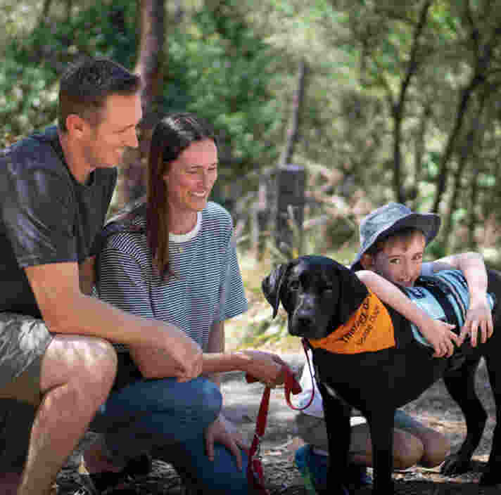 A young boy cuddling a black Therapy Dog, while his parents watch on smiling.