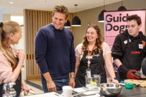 Curtis Stone smiles at a Client during a cooking class with a Guide Dogs staff present.