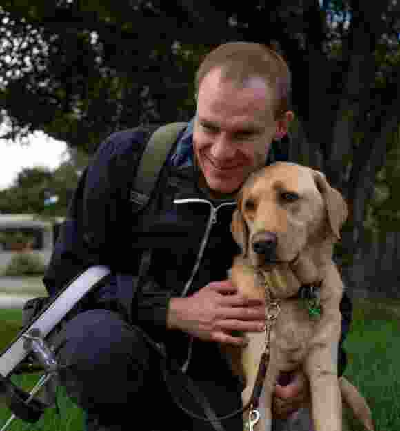 Brendan a GDV ambassador is hugging his Guide Dog Gunner outside in the park.