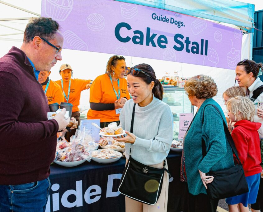 Patrons of the Guide Dogs Community Fair cake stall, queuing and buyings sweets.