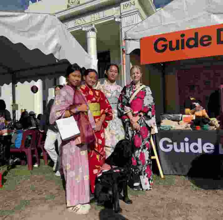 Four attendees wearing colourful kimonos at the Japan Festival 2025, with a black guide dogs wearing a harness.