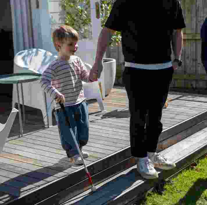 Louis holding hands with his father along side his mother using his cane to navigate the steps from the backyard patio to the grass.