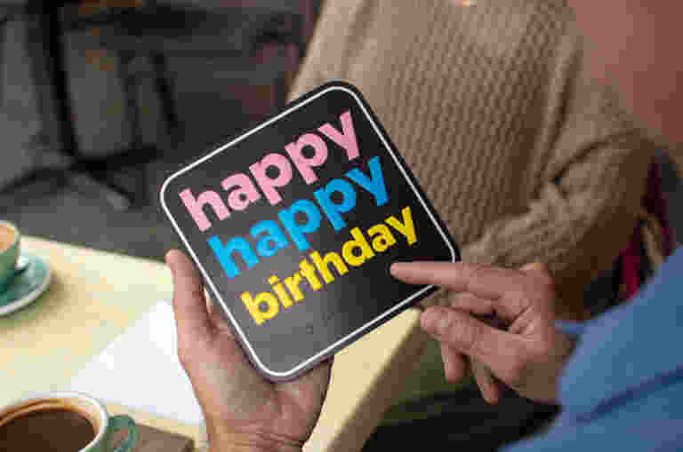 A person holding a birthday card that says "happy happy birthday" in colourful letters with braille embossed underneath the text