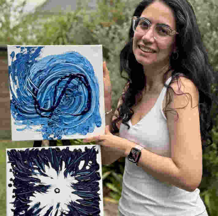Noora Remi smiling holding up two pieces of her artwork.