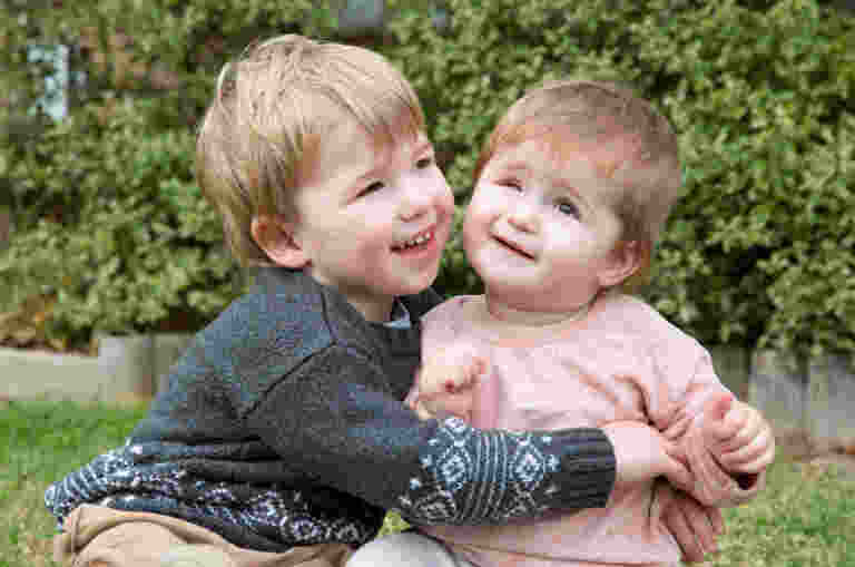 Young boy hugs his little sister Abigail who has a vision impairment as they play in their backyard.