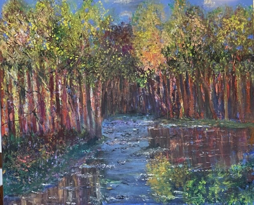 A colorful autumn forest with tall trees lining a flowing river that reflects the vibrant reds, oranges, yellows, and greens of the foliage and sky.