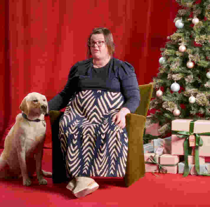 Gemma sitting in front of a Christmas tree and presents with Therapy Dog Keith