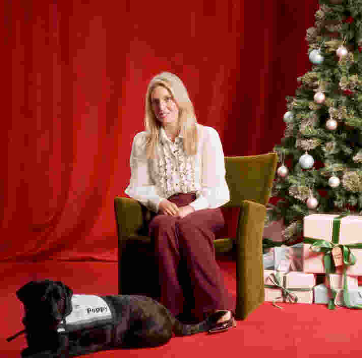 Judge Amanda Mansini sitting in front of a Christmas tree and presents with Court Dog Poppy