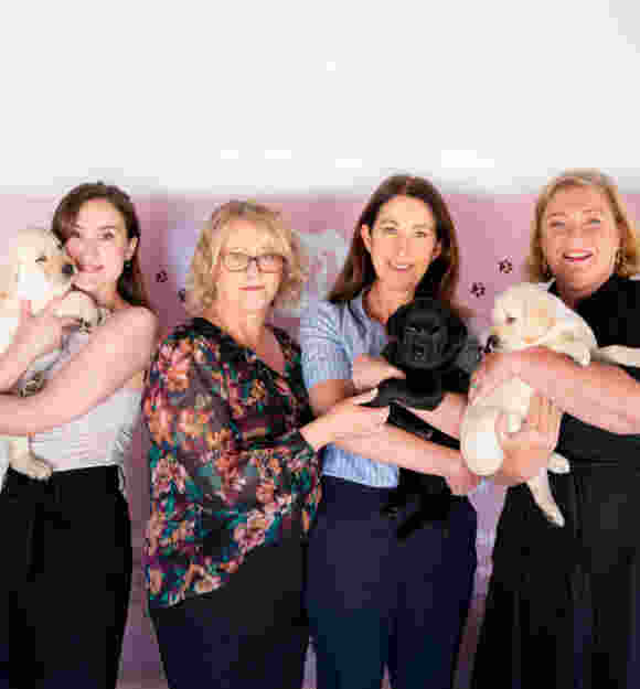 Melanie, Josie, Katie and Cath smiling at the camera holding a mix of black and yellow lab puppies.