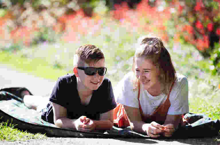 Guide Dogs Client Lindsay and sister laying next to each other on a picnic rug in the grass.