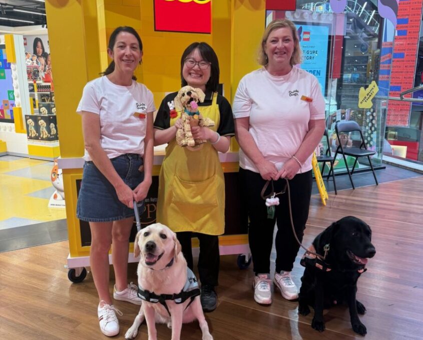 Katie and Cath standing with Ambassador Dogs Keith and Gizmo at the Lego Launch with a LEGO staff member.