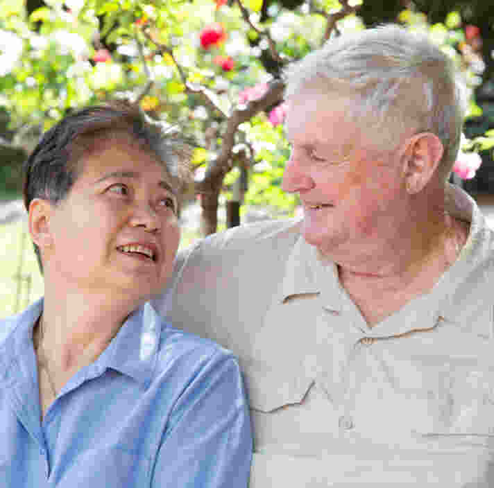 An older couple in a garden setting look into each others eyes.