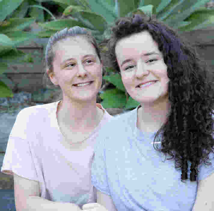 Two female school students in a garden setting, sitting with linked arms.