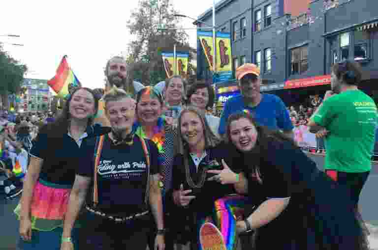 Guide Dogs clients, staff members and the audio describers from the MCA at the Sydney Gay and Lesbian Mardi Gras wearing rainbow coloured clothes and accessories
