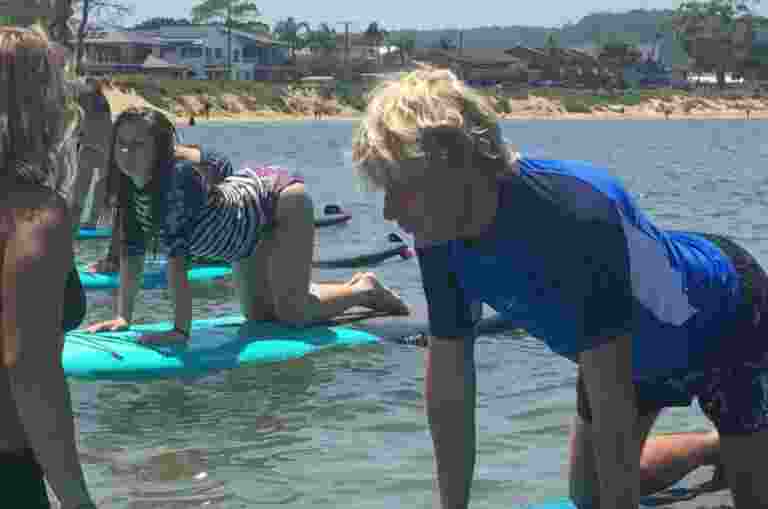 Two young clients, kneeling on paddle boards in the water