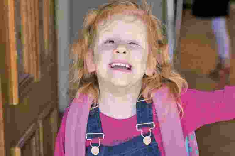 A young client with her backpack on, smiling to camera as she leaves her front door.