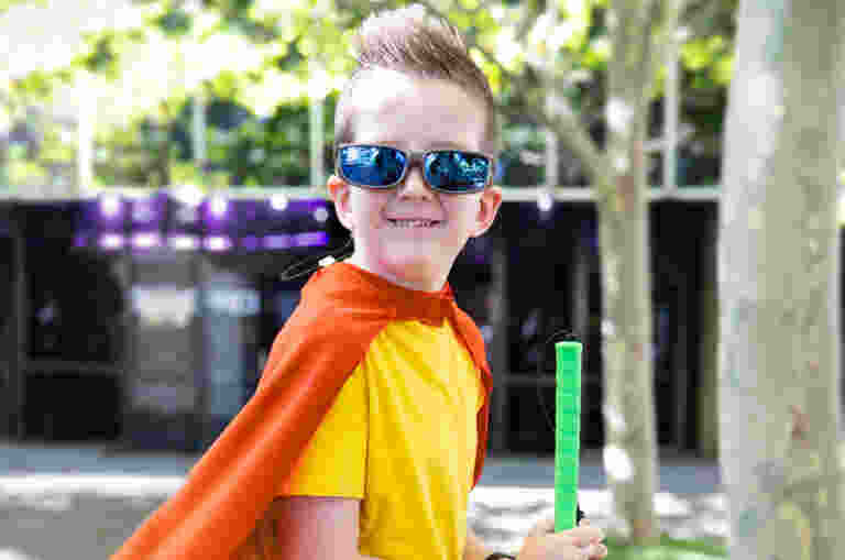 A child wearing a red superhero cape, proudly holding a cane