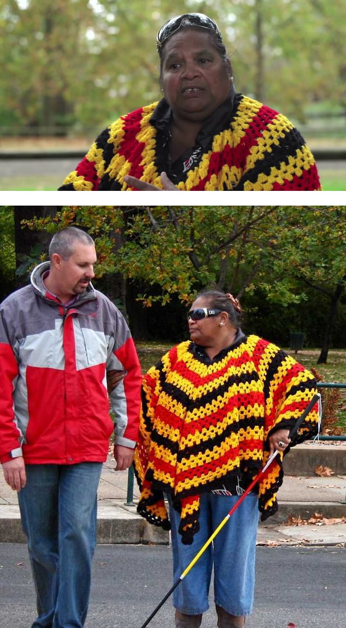 Aunty Mary wearing a knitted poncho in black, red and yellow, using her cane to help cross the road