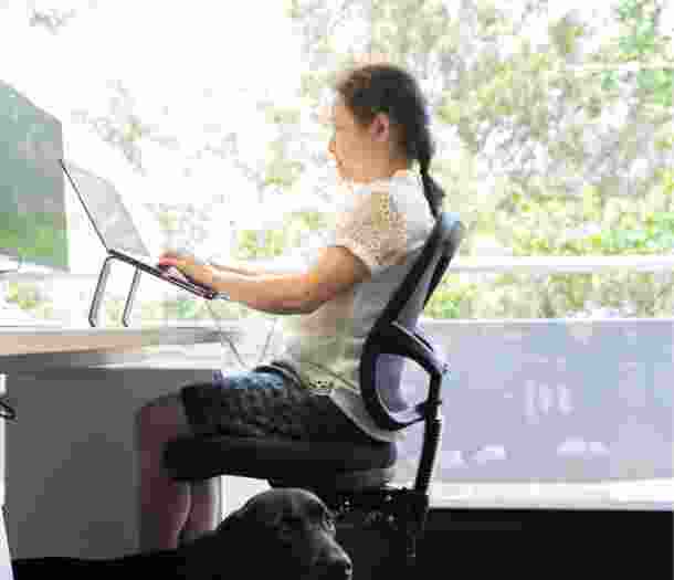 A person sitting at a desk using their laptop. The image is a profile view.