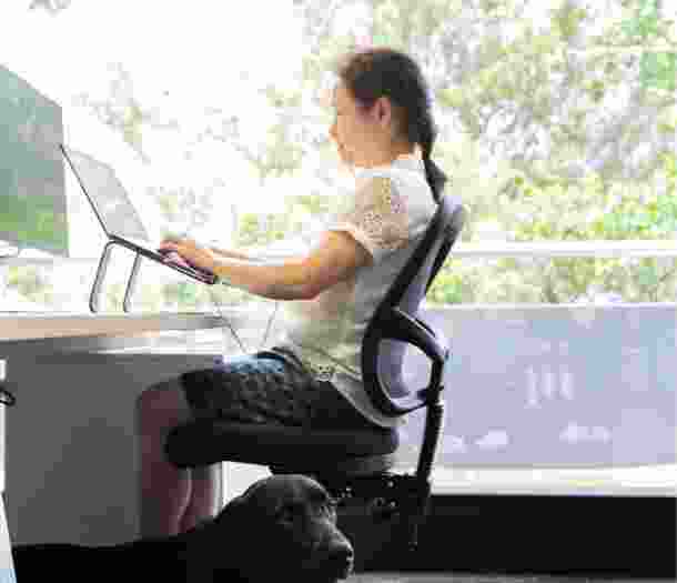 A person sitting at a desk using their laptop. The image is a profile view.