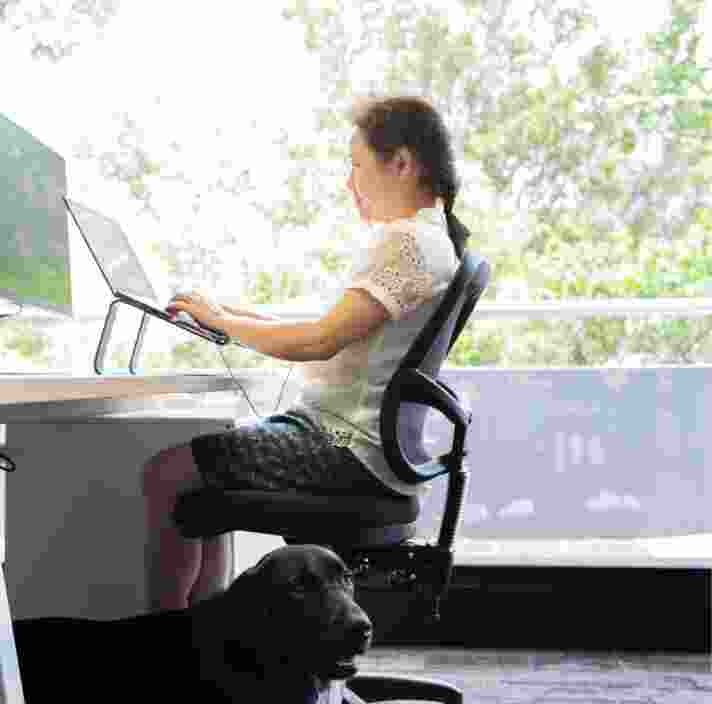 A person sitting at a desk using their laptop. The image is a profile view.