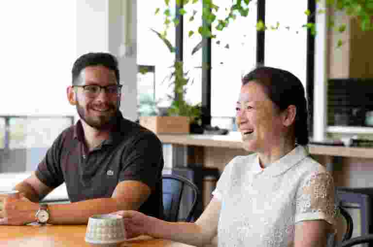 Two people sitting at cafe table. Both people are smiling.