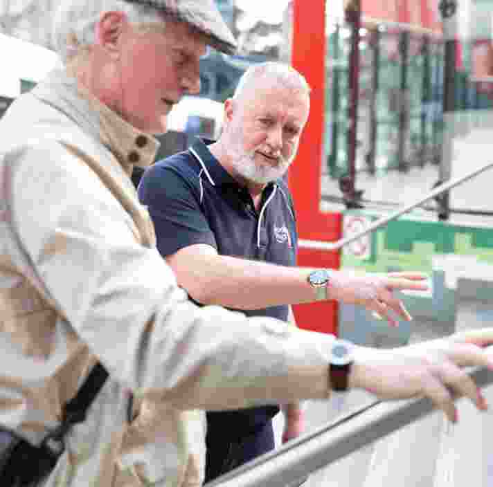A Guide Dogs staff member assisting an an older adult with navigating a handrail.