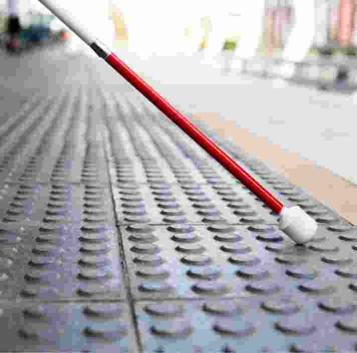 Close up image of the bottom half of a white cane on tactile tiles.