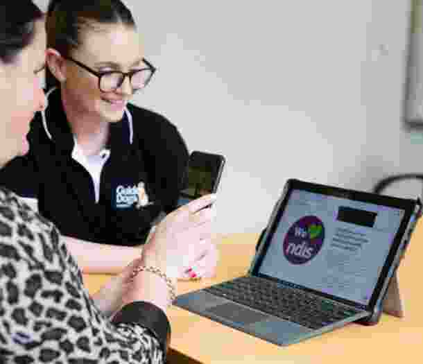 A person and a Guide Dog's staff member looking at a laptop. The person is holding up an Iphone to the laptop and the staff member is smiling.